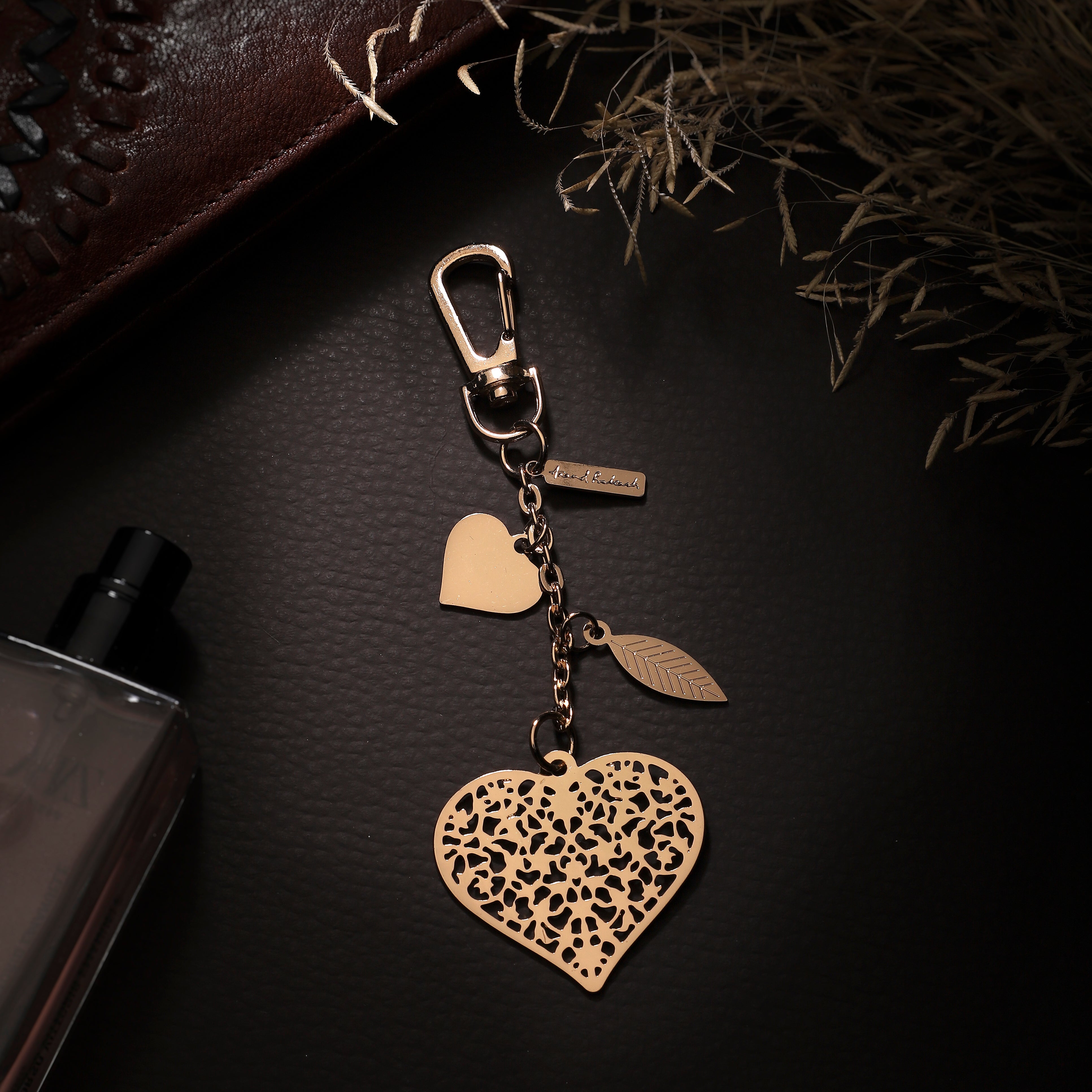 A gold-colored metal bag charm with a heart pattern, electroplated for a shiny finish, attached to a keychain ring. The charm is displayed on a dark background.